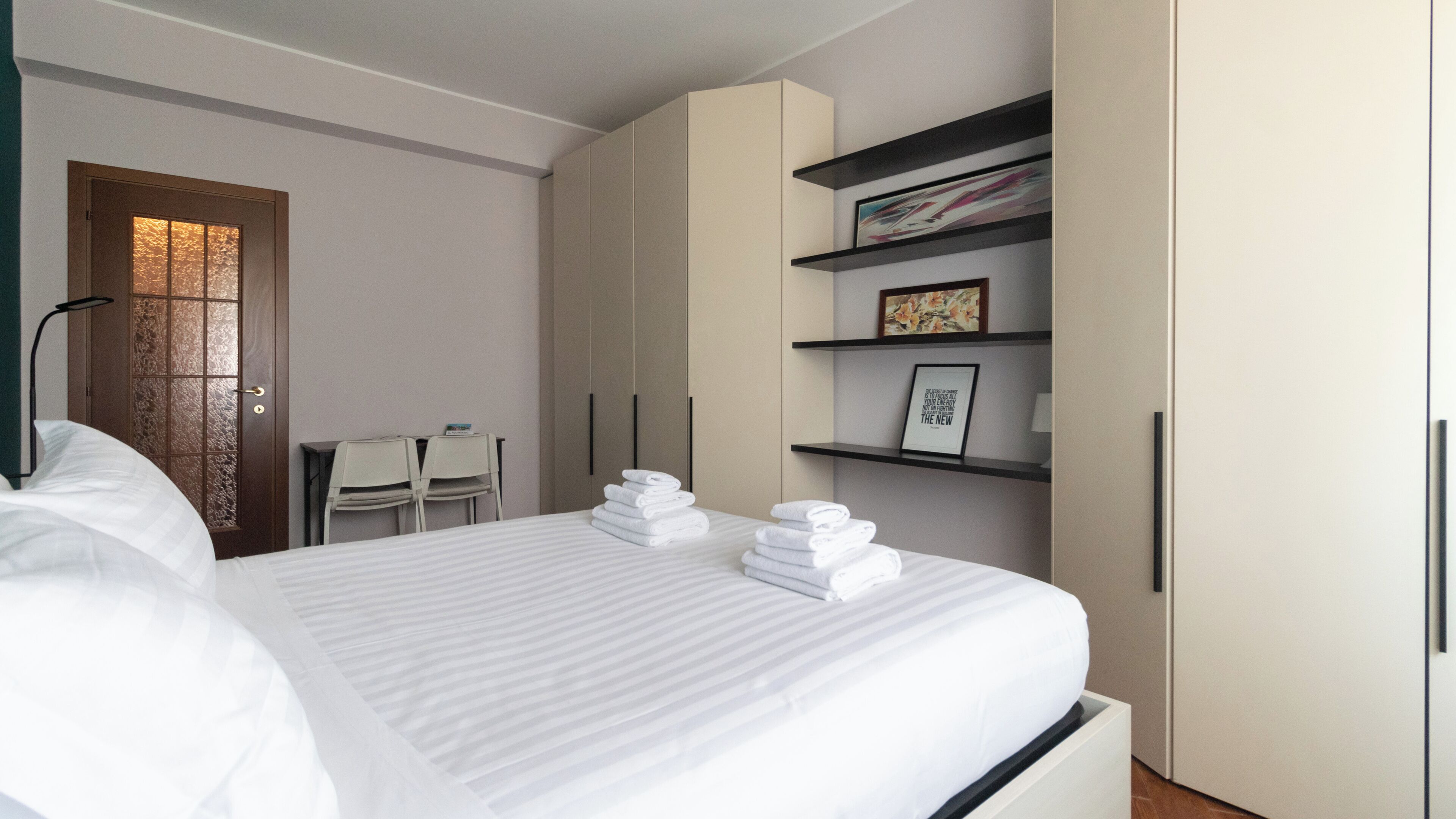 Una habitación de hotel moderna con una cama bien hecha, un escritorio con sillas y un armario con estantes.