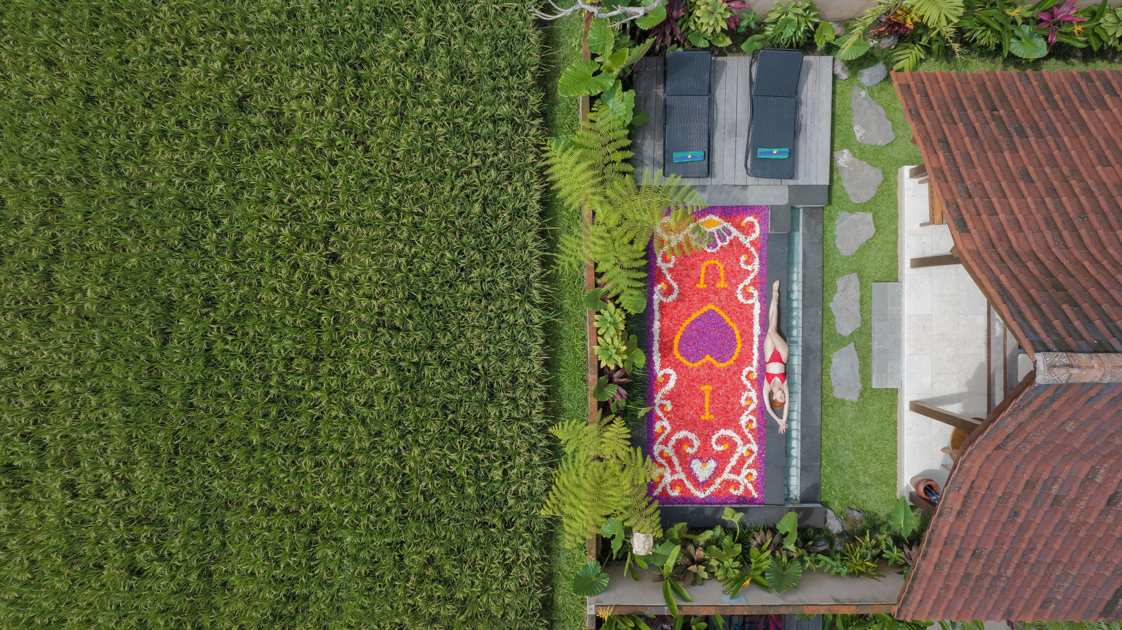 An aerial view of a property with a green lawn, a patterned outdoor area with lounge chairs, and a tiled roof structure.