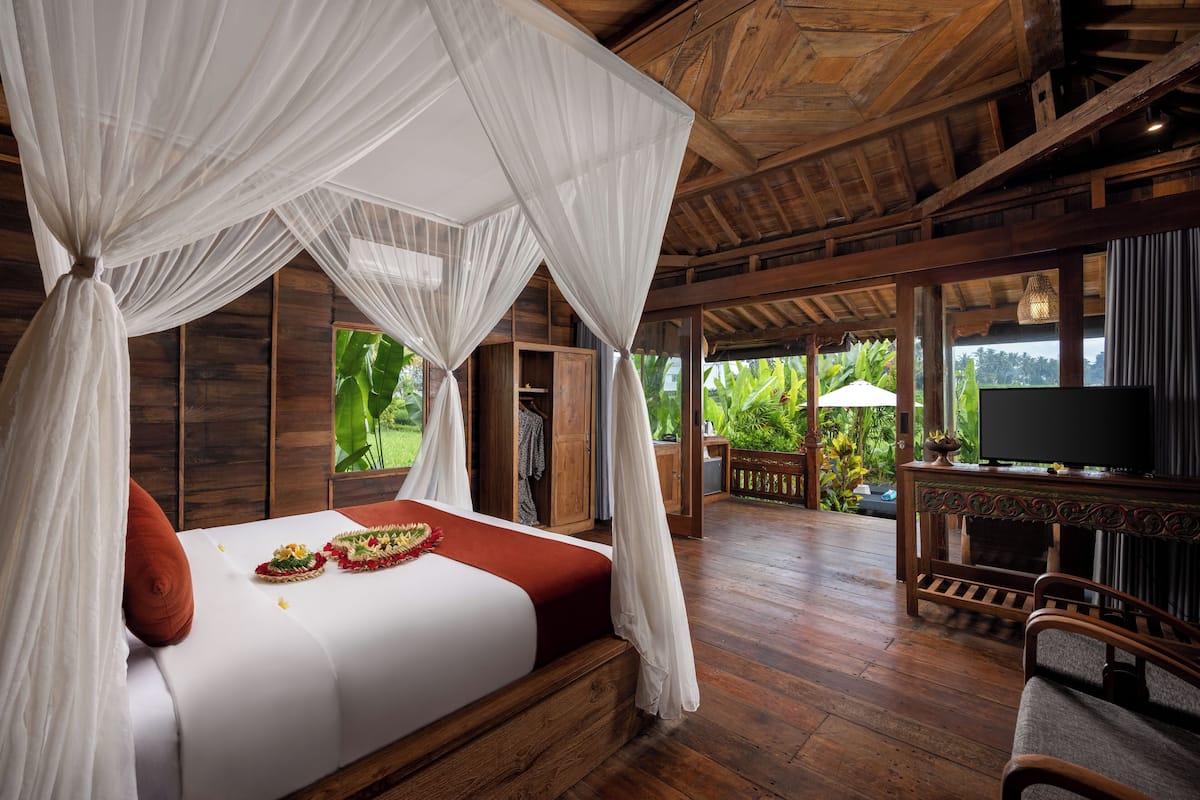 A wooden-framed room with a bed, a TV, and a view of greenery.