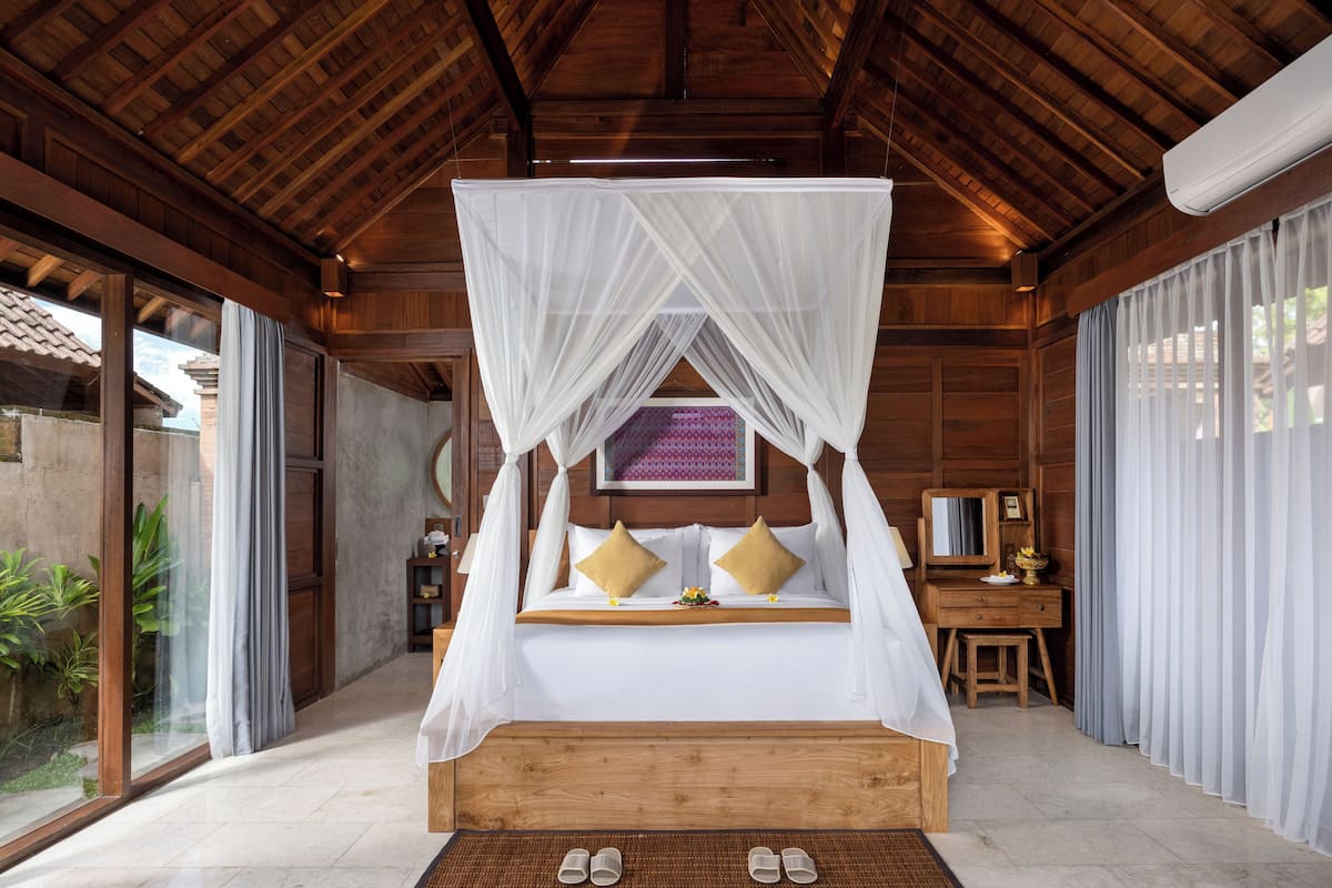 A room with a bed under a canopy, a wooden desk, and a large window.