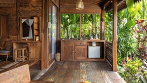 Una habitación rústica de madera con una cama, una mesita con un florero y vistas a vegetación exuberante.