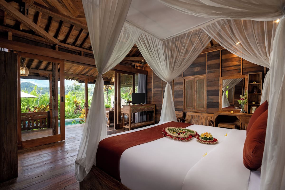A spacious bedroom with a large bed, wooden furniture, and a view of lush greenery.