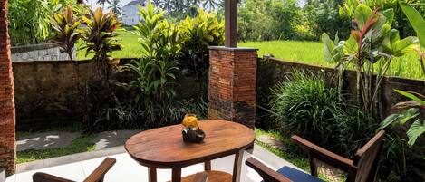 A round wooden table with two chairs, surrounded by lush greenery and a brick wall.