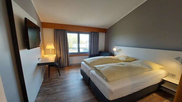 Een hotelkamer met een bed, nachtkastjes, een bureau, een stoel, een televisie en een raam met gordijnen.