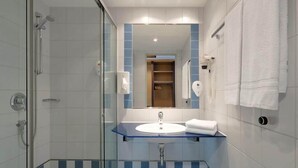 Een moderne badkamer met een douchecabine van glas, een blauw geruit vloertje, een witte wastafel en een grote spiegel.