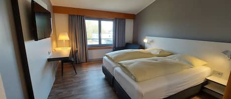 Una habitación de hotel con cama, mesitas de noche, un escritorio, una silla, televisión y ventana con cortinas.