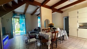 Uma sala de jantar com uma mesa posta para quatro pessoas, um sofá e uma cozinha com armários.