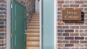 Une porte verte donnant sur un escalier en bois, un mur de briques et une pancarte indiquant « Jarvie Cottage ».