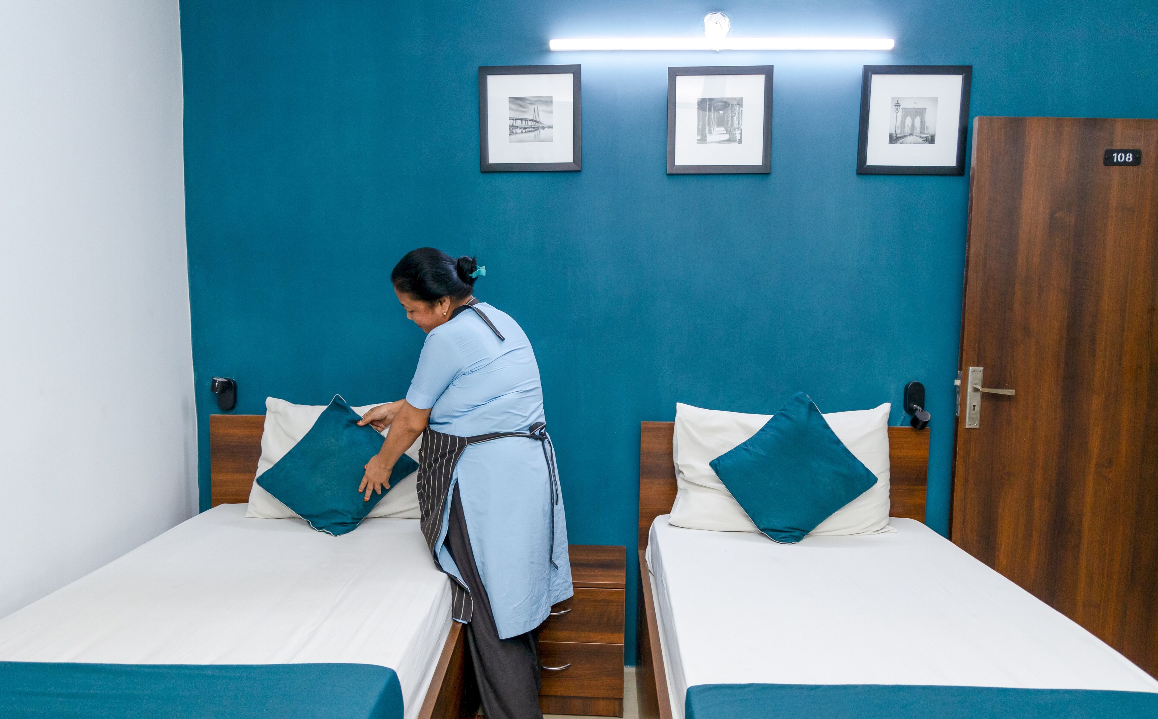 Een hotelkamer met twee bedden, blauwgroene beddengoed, een houten garderobe en ingelijste foto's aan de muur.