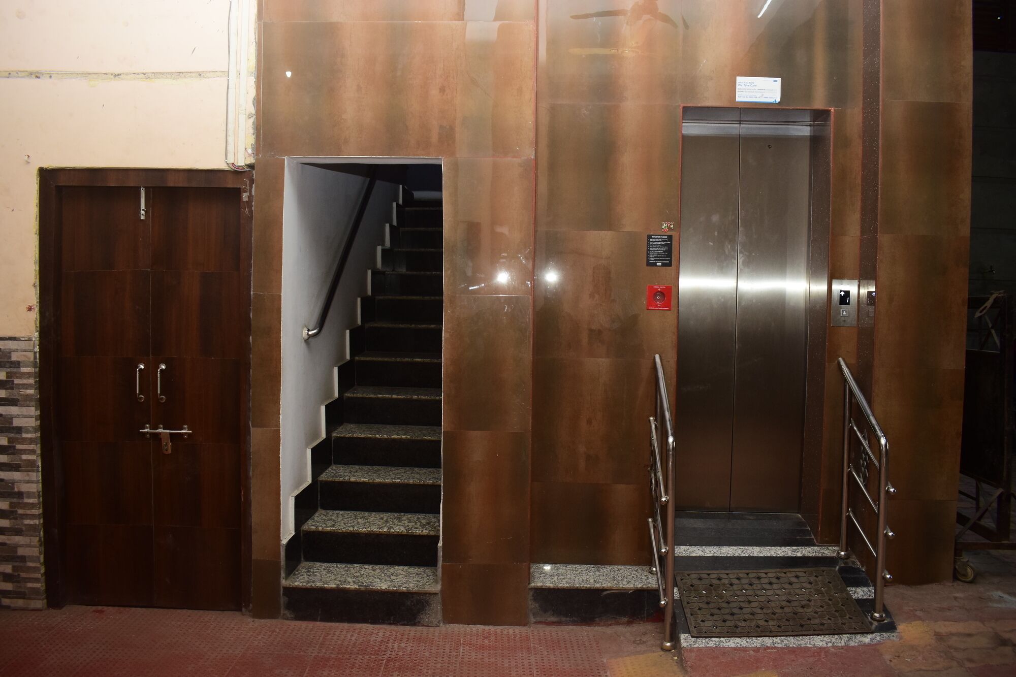 A set of stairs leading to an elevator, with a wooden door on the left and a metal elevator door on the right.