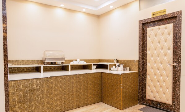 Une petite pièce bien éclairée, avec un comptoir de buffet, une porte ornée d’un panneau capitonné et un panneau indiquant l’emplacement des toilettes.