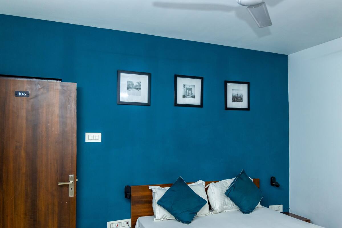 Une pièce avec une porte en bois, un lit avec une literie blanche et des coussins turquoise, et trois tableaux encadrés accrochés au mur.