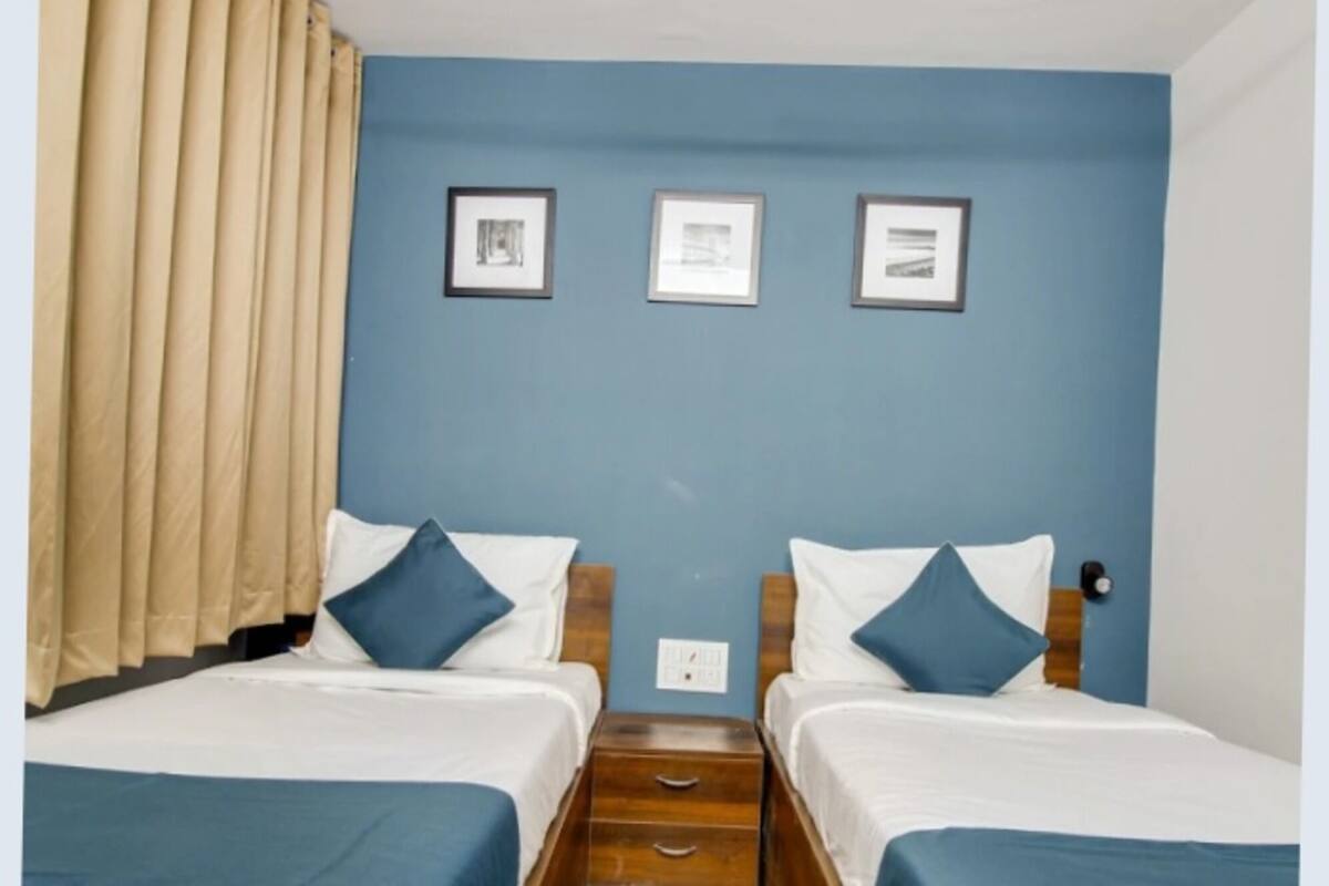 Une chambre d’hôtel avec deux lits, des rideaux de couleur beige et trois tableaux encadrés accrochés au mur.