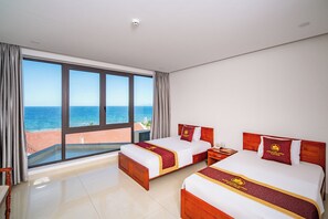 Habitación de hotel con dos camas, amplias ventanas con vista al mar y un balcón.