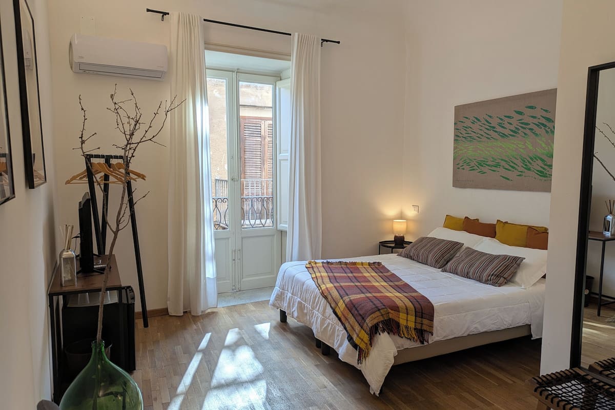 Ein Schlafzimmer mit Bett, Nachttisch, Lampe und Blick auf den Balkon.