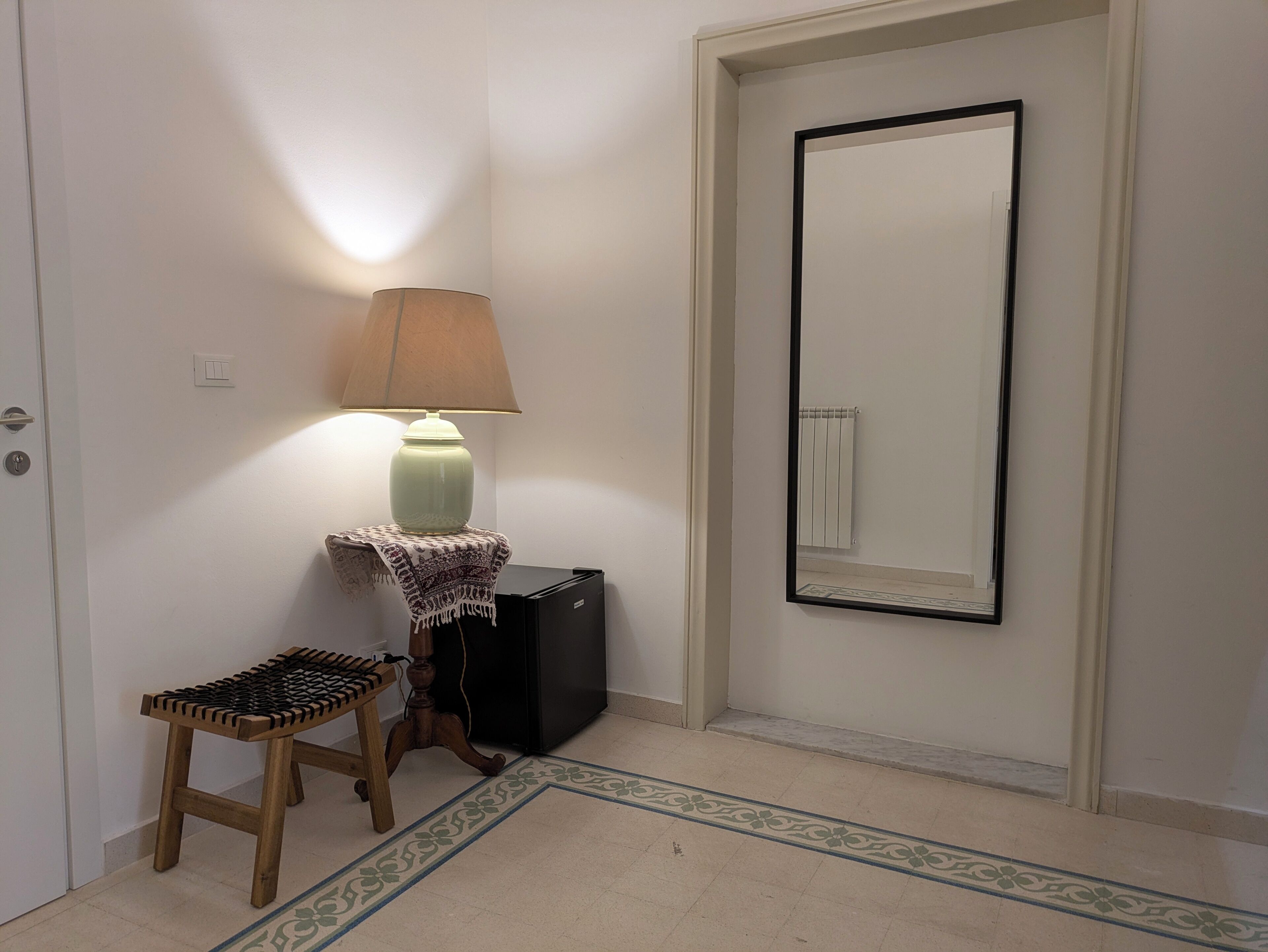 A hallway with a lamp, a small stool, a mirror, and a radiator.