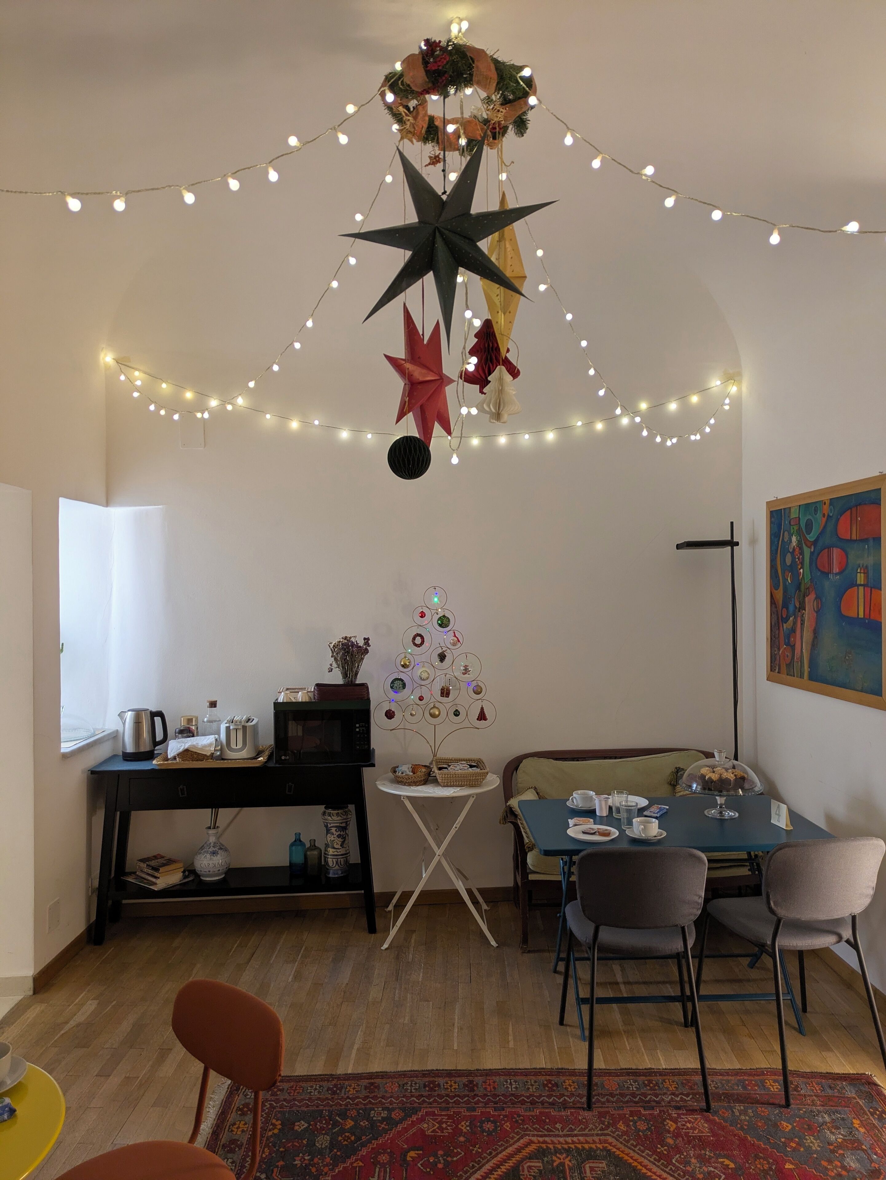 A cozy living room with a star decoration, string lights, a small Christmas tree, and a dining area with chairs and a table.