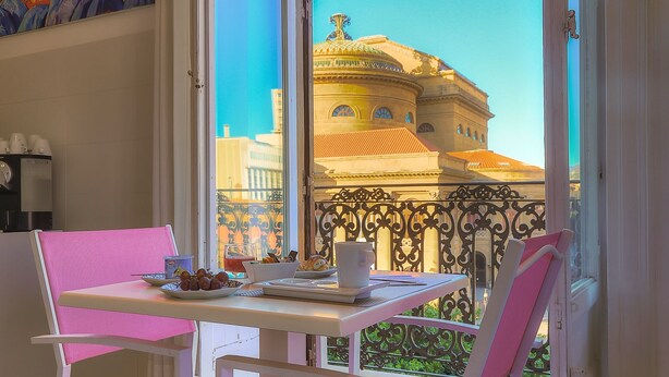 A balcony with a table set for two, a decorative railing, and a view of a historic building. - Palco Rooms&Suites (Palermo)