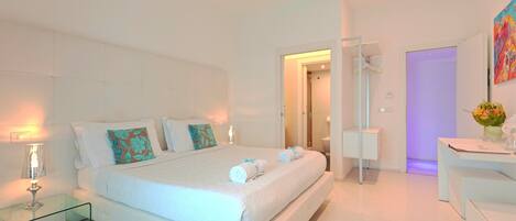 A modern bedroom with a large bed, bedside tables, a desk, and a bathroom visible through an open door.