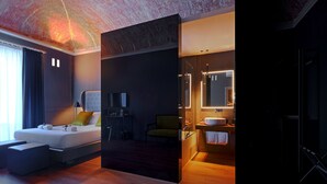 A modern hotel room with a large bed, a sitting area, a bathroom with a large mirror, and a wooden floor. - Palco Rooms&Suites (Palermo)