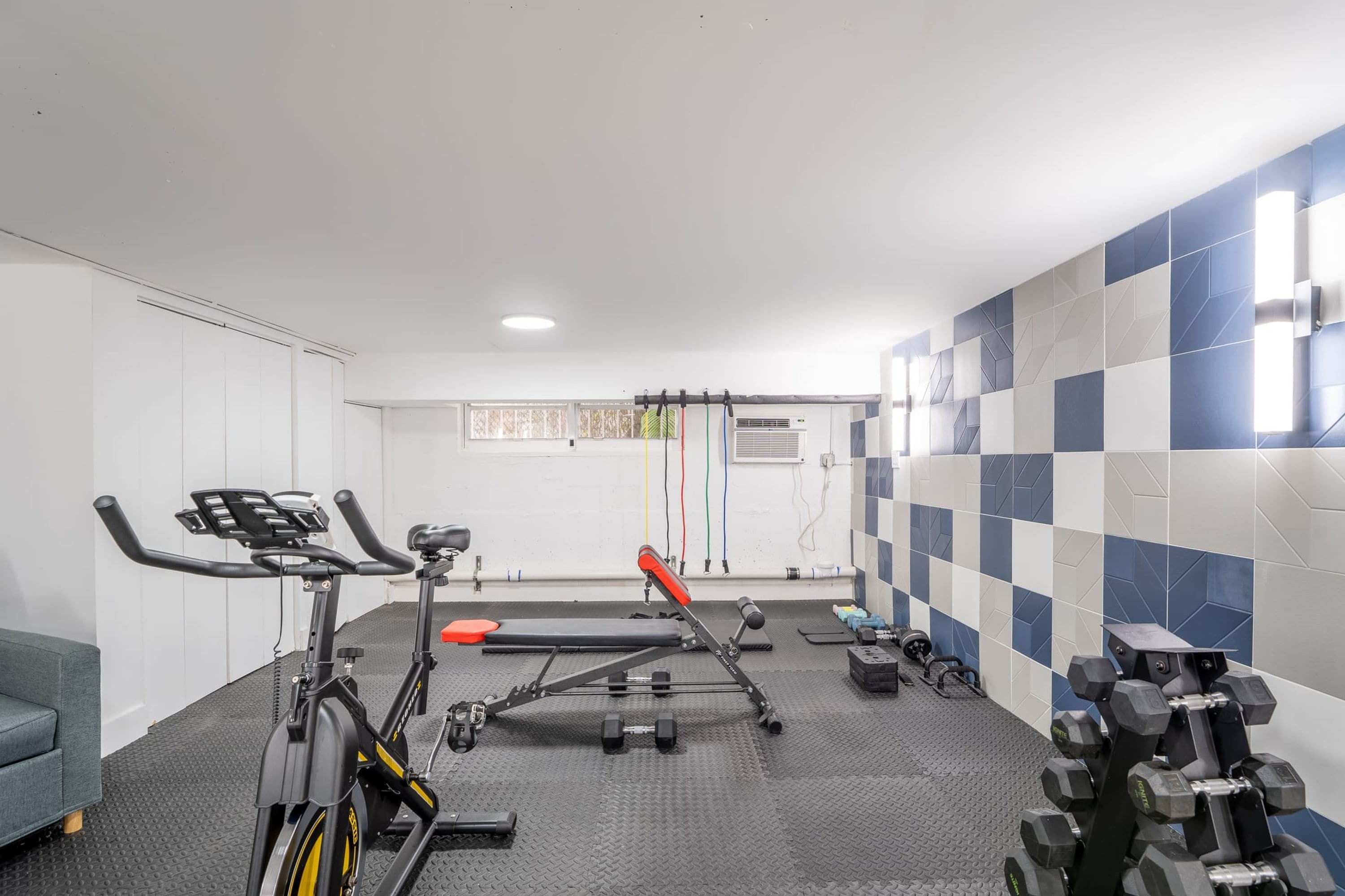 A gym with exercise equipment, a bench, and a wall with a checkered pattern.