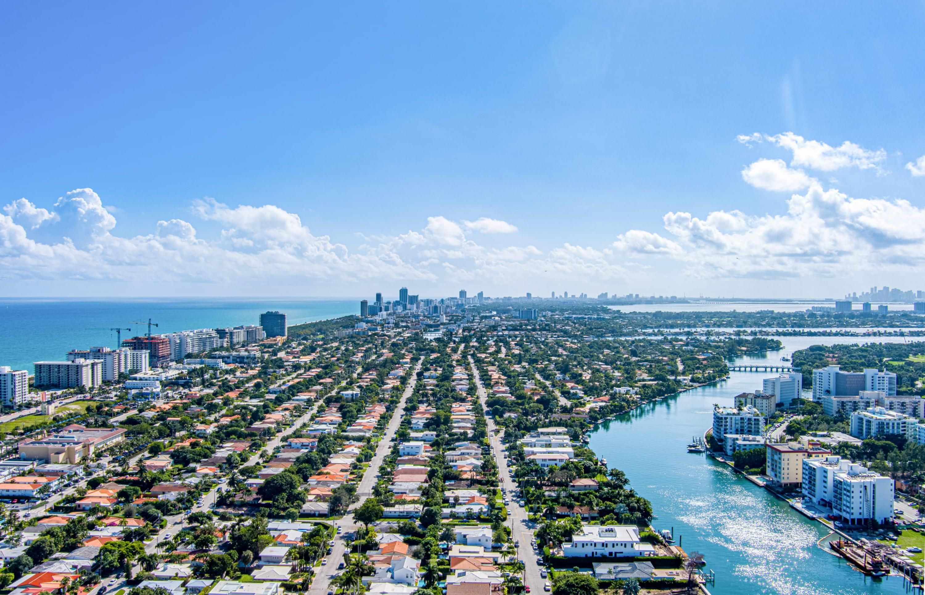 A coastal cityscape with dense residential areas, a marina, and a bridge connecting to the mainland.