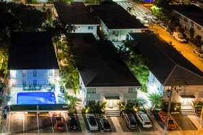 An aerial view of a residential area with multiple houses, a swimming pool, and parked cars.