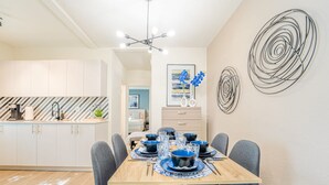 A modern dining area with a wooden table set for six, grey upholstered chairs, and a contemporary light fixture above. - TWO Bedroom Apartment (Miami Beach)