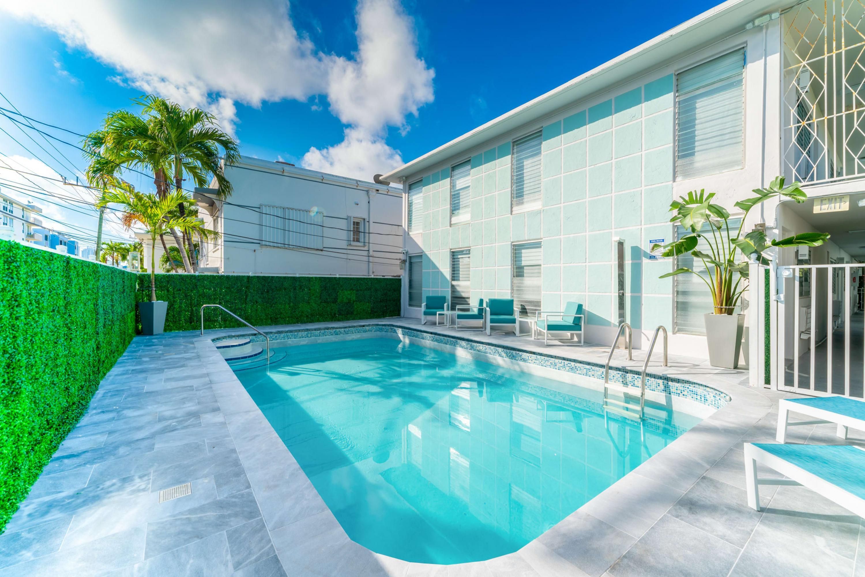 Une piscine entourée d’une terrasse carrelée, de chaises longues et d’une haie verdoyante.