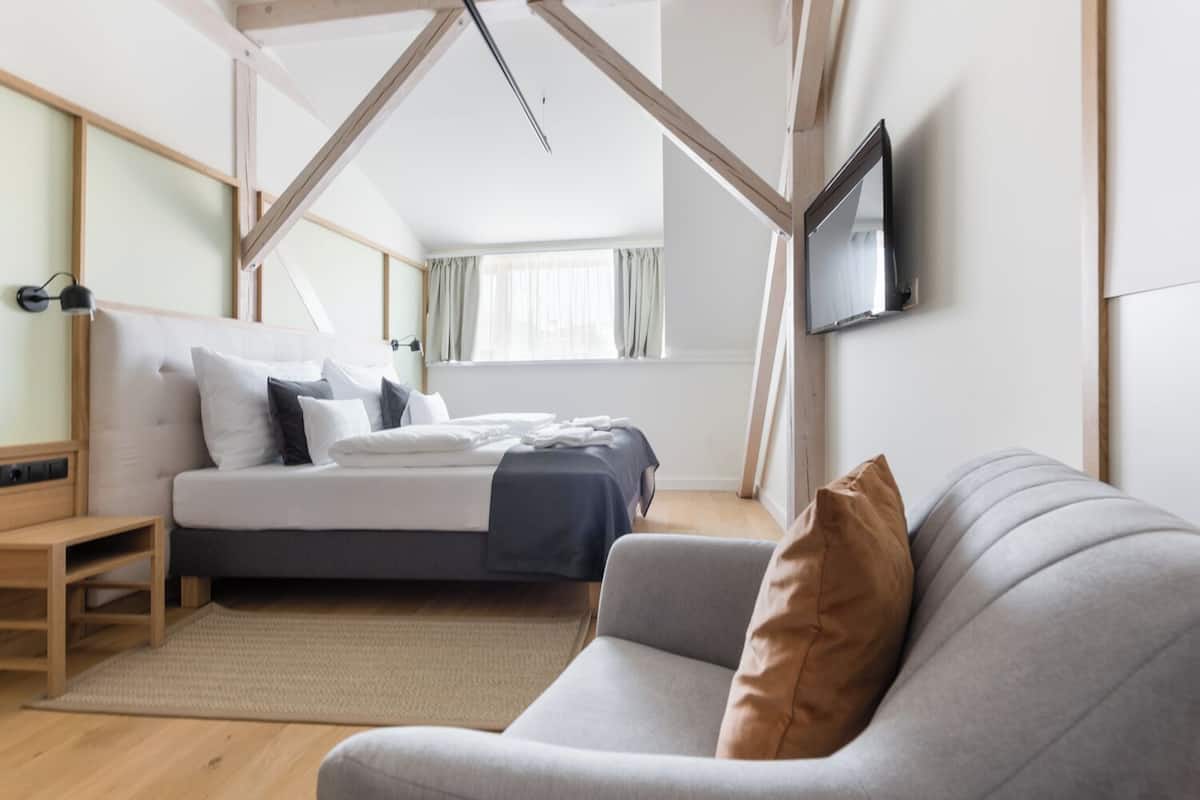 Et moderne soveværelse med seng, sofa, fjernsyn og et træloftsdesign.