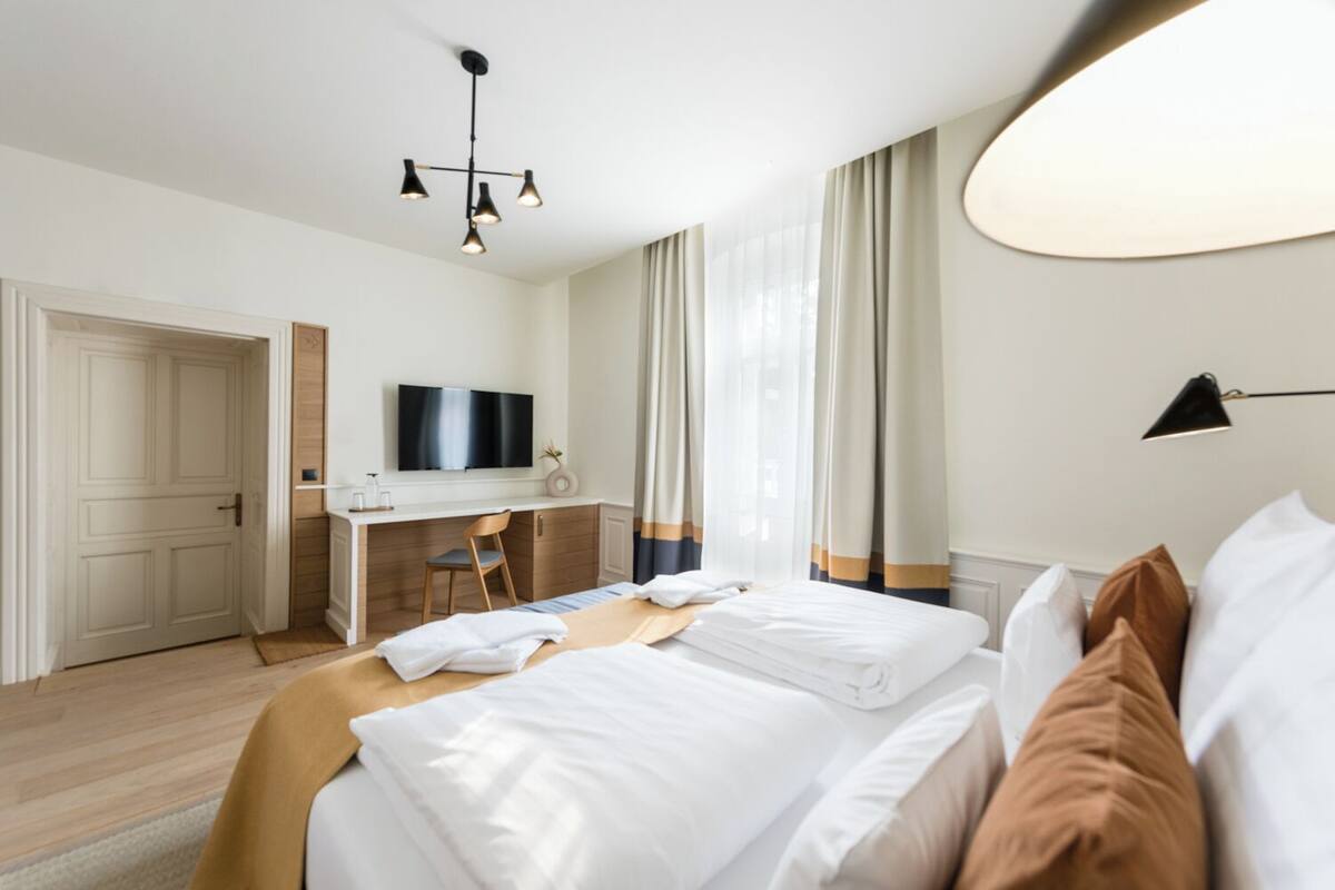 Et hotelværelse med seng, skrivebord, stol, fjernsyn og et vindue med gardiner.