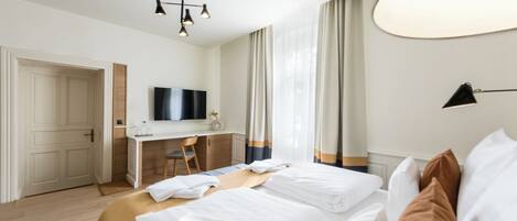A hotel room with a bed, a desk, a chair, a TV, and a window with curtains.