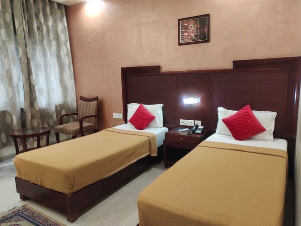 A hotel room with two single beds, a wooden headboard, a small table, and a chair. - Hotel RKV Residency (Krishnagiri)