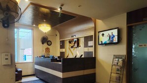A hotel reception area with a reception desk, a chandelier, a clock, a television, and a sign indicating the way to the Indian Express. - Hotel RKV Residency (Krishnagiri)