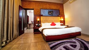 A hotel room with a large bed, wooden headboard, bedside lamps, and a herringbone-patterned floor. - Hotel RKV Residency (Krishnagiri)