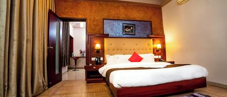 A hotel room with a large bed, wooden headboard, bedside lamps, and a herringbone-patterned floor.