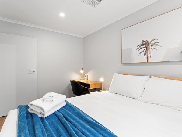 A modern hotel room with a neatly made bed, a desk with a lamp, and a framed picture on the wall.