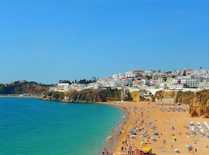 Une plage avec des bâtiments situés sur une colline en arrière-plan.