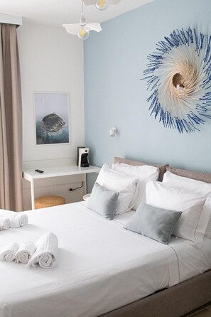 A neatly made bed with white and gray pillows, a white desk with a coffee maker, a wall-mounted lamp, and a framed picture on the wall. - Delphis Pula rooms (Pula)