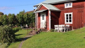 A red wooden house with a white door and windows, a porch with white chairs, and a small garden area. - Cozy and spacious traditional Swedish Dala cottage (Dalarnas län)