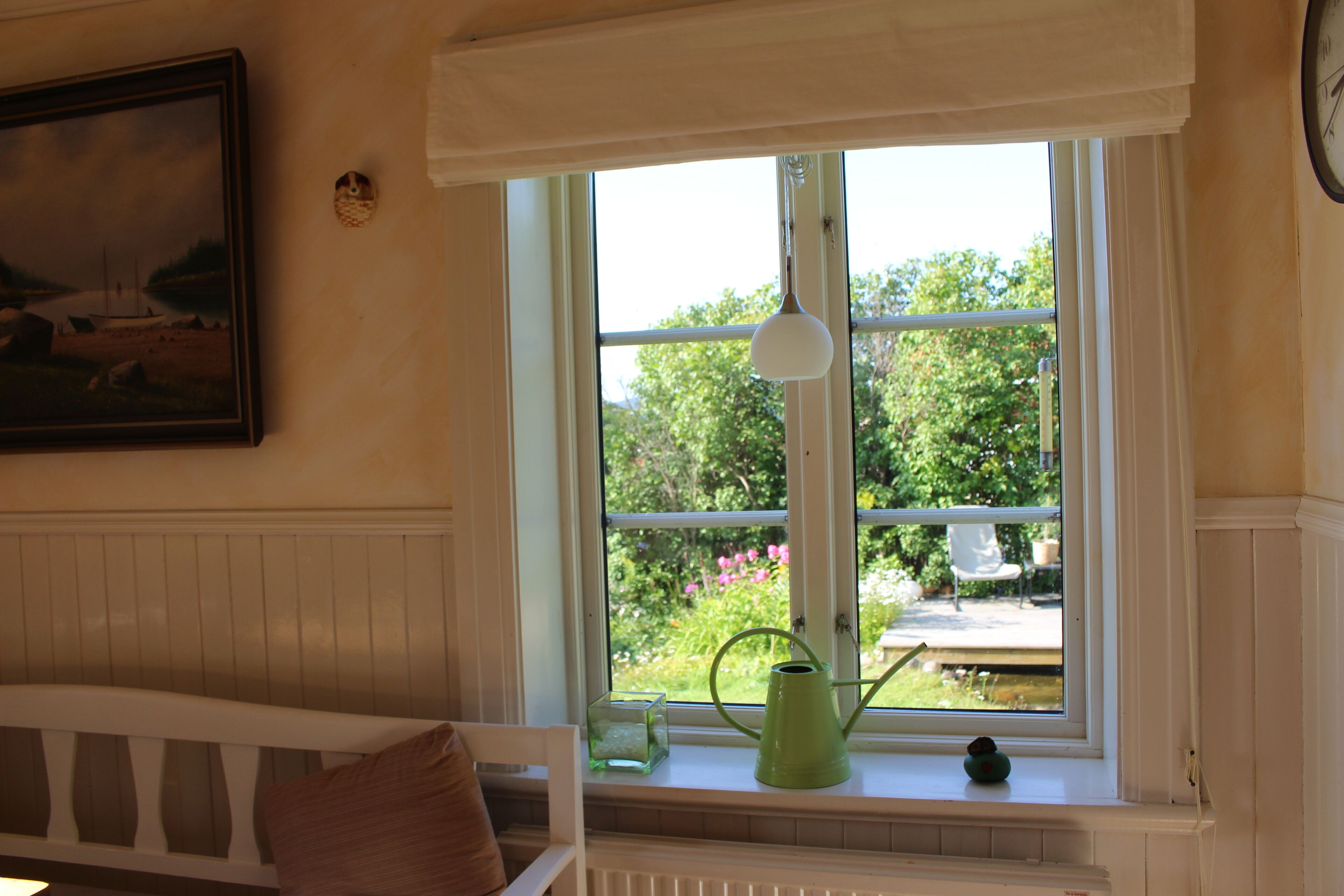 Et værelse med et vindue, en grøn vandkande, en hvid radiator og et billede i ramme på væggen.
