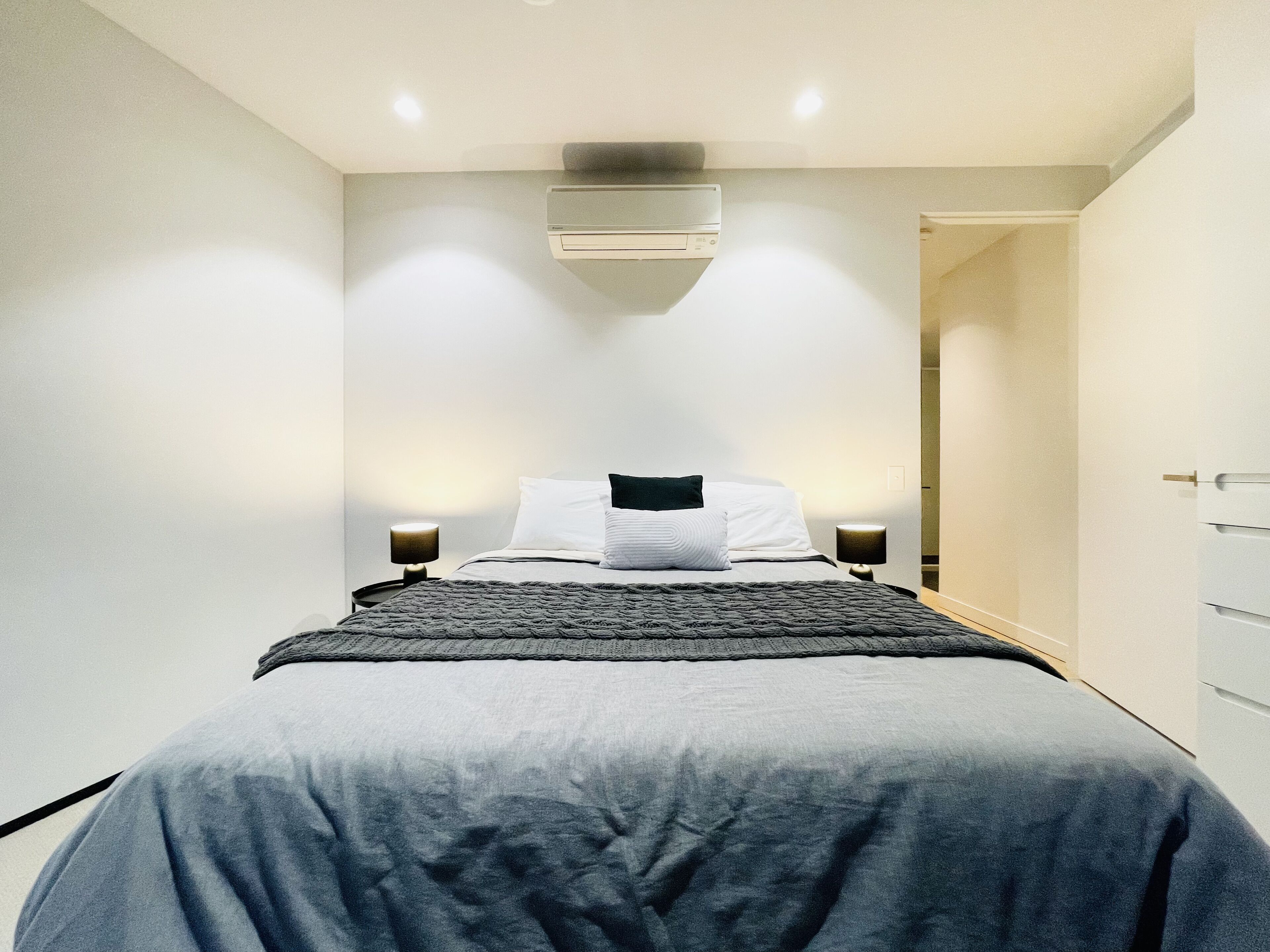 A modern bedroom with a bed, bedside lamps, and a ceiling-mounted air conditioner.