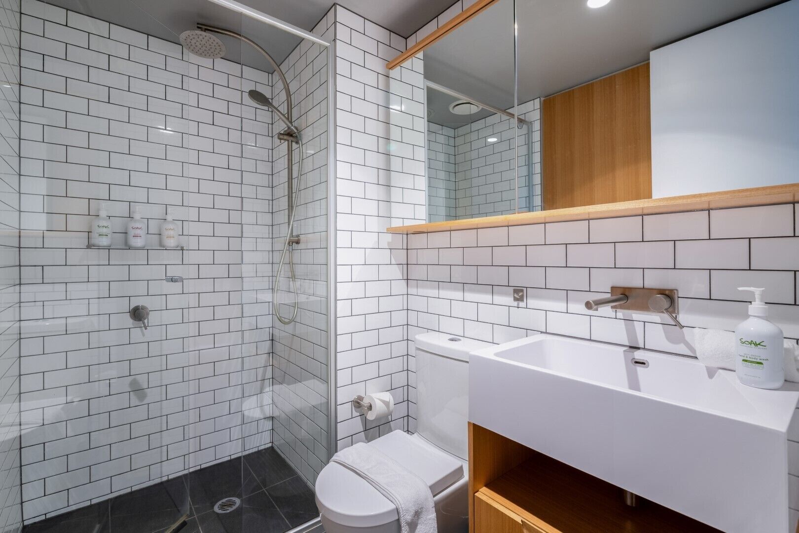 A modern bathroom with white subway tiles, a glass-enclosed shower, a wooden vanity, and a white toilet.