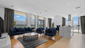 Ein modernes Wohnzimmer mit einer blauen Sofagarnitur, einem Couchtisch und Blick auf die Stadt durch große Fenster.
