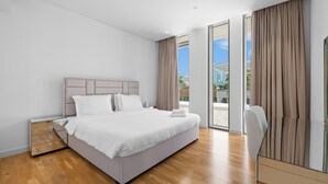 Ein modernes Hotelzimmer mit einem großen Bett, einem Nachttisch und einer Glastür, die auf einen Balkon führt.