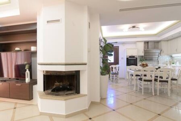 Una sala de estar moderna con chimenea, un comedor con sillas blancas y una cocina al fondo.