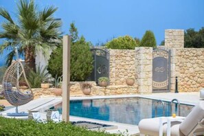 Un área de piscina con una pared de piedra, una silla colgante y sillones de descanso.