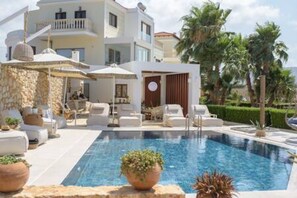 Zona de piscina con sillas de descanso, un muro de piedra y un edificio con balcones.