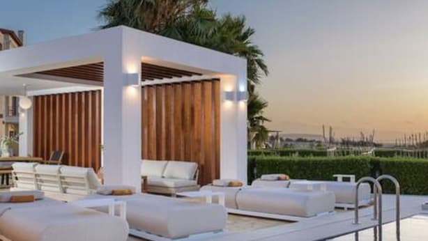 A modern outdoor lounge area with seating and a pool, surrounded by greenery and palm trees. - Therros Villa With Private Pool by Estia (Hersonissos)