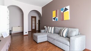A modern living room with a grey sectional sofa, wooden flooring, a white cabinet, and a door leading to another room. - Italianway Easy - Lecchi 20 (Milan)